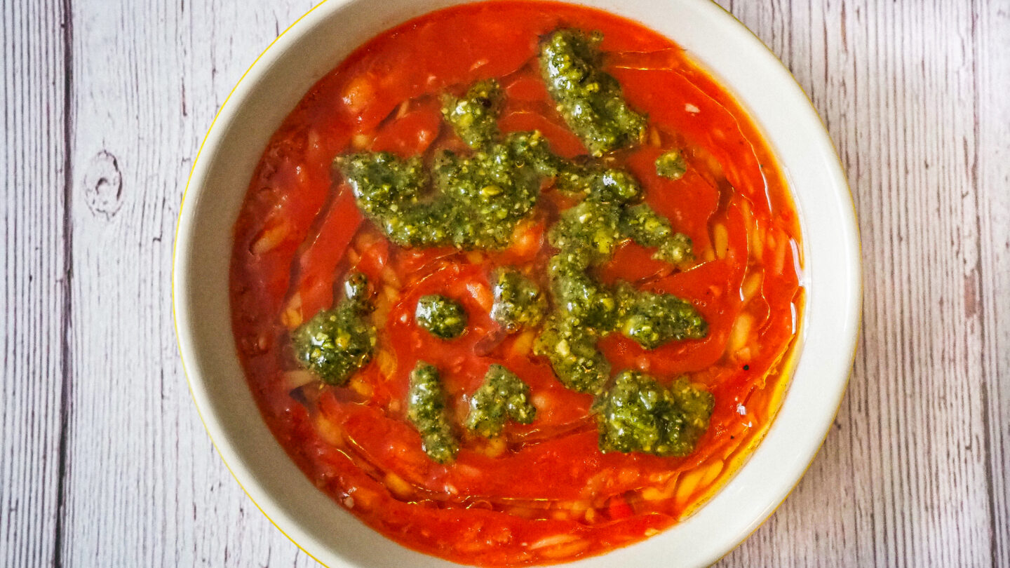 Bowl of tomato, chickpea & orzo soup with Pistachio Pesto on a rustic white wooden background