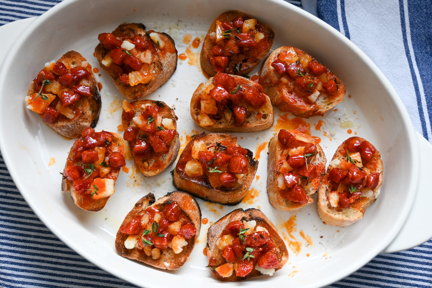 Honey Glazed Chorizo with Manchego Cheese on small slices of toasted baguette on a white dish with a blue & white striped background