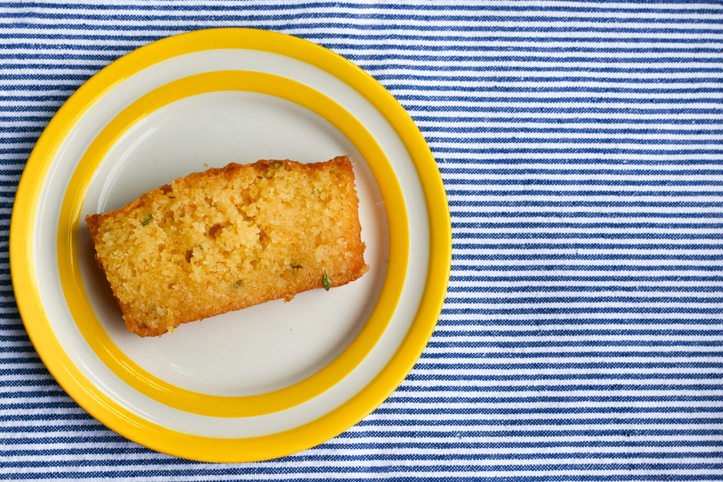 Slice of yellow Lemon & Thyme Loaf Cake on a striped yellow Cornishware dessert plate on a blue & white striped background