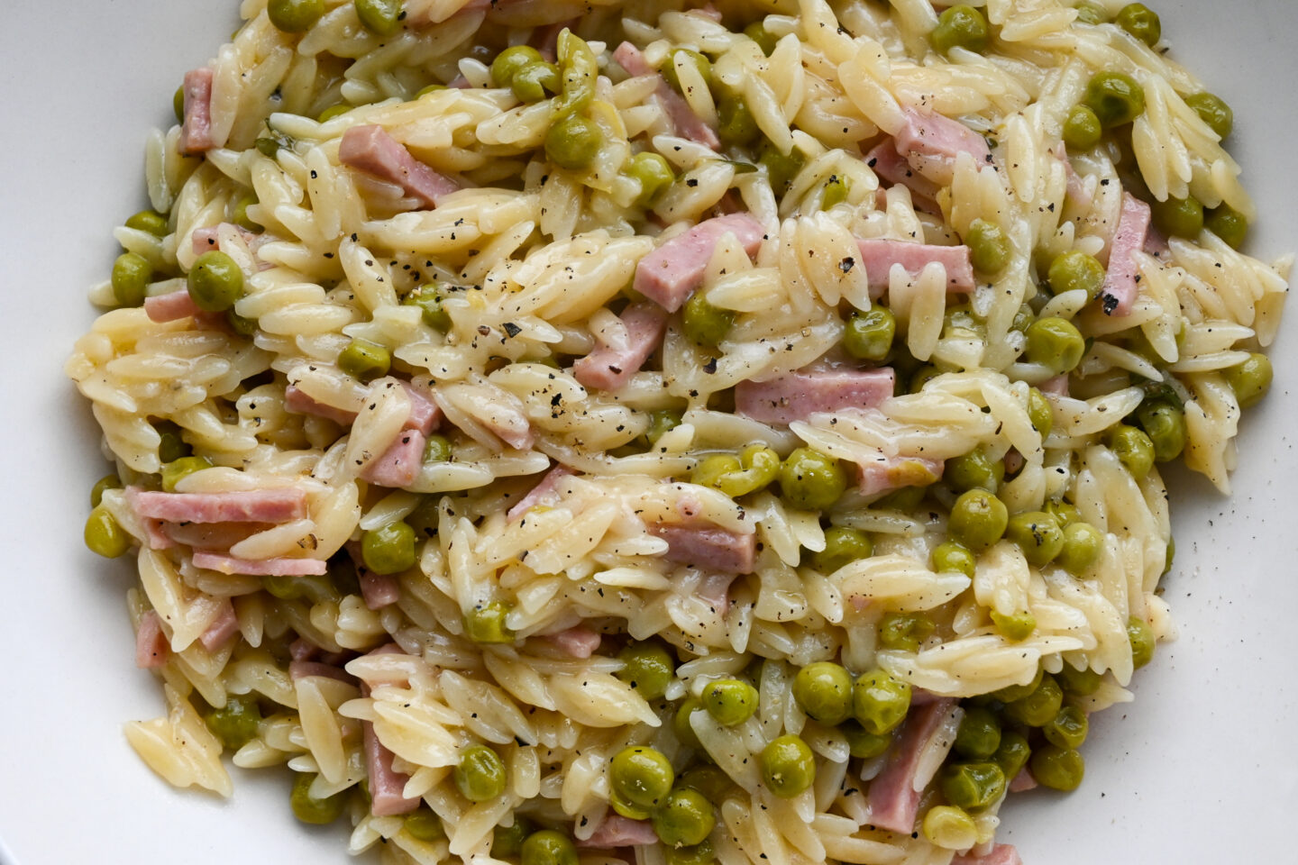 Closeup of bowl of orzo, ham cubes & peas on a blue and white striped background
