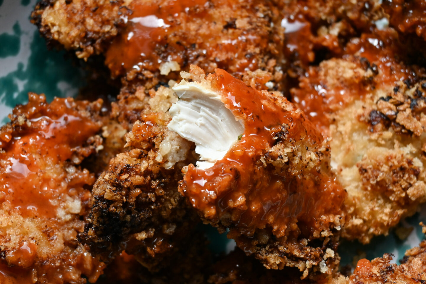 Buffalo drizzled fried chicken tender torn in half to reveal the white chicken meat inside