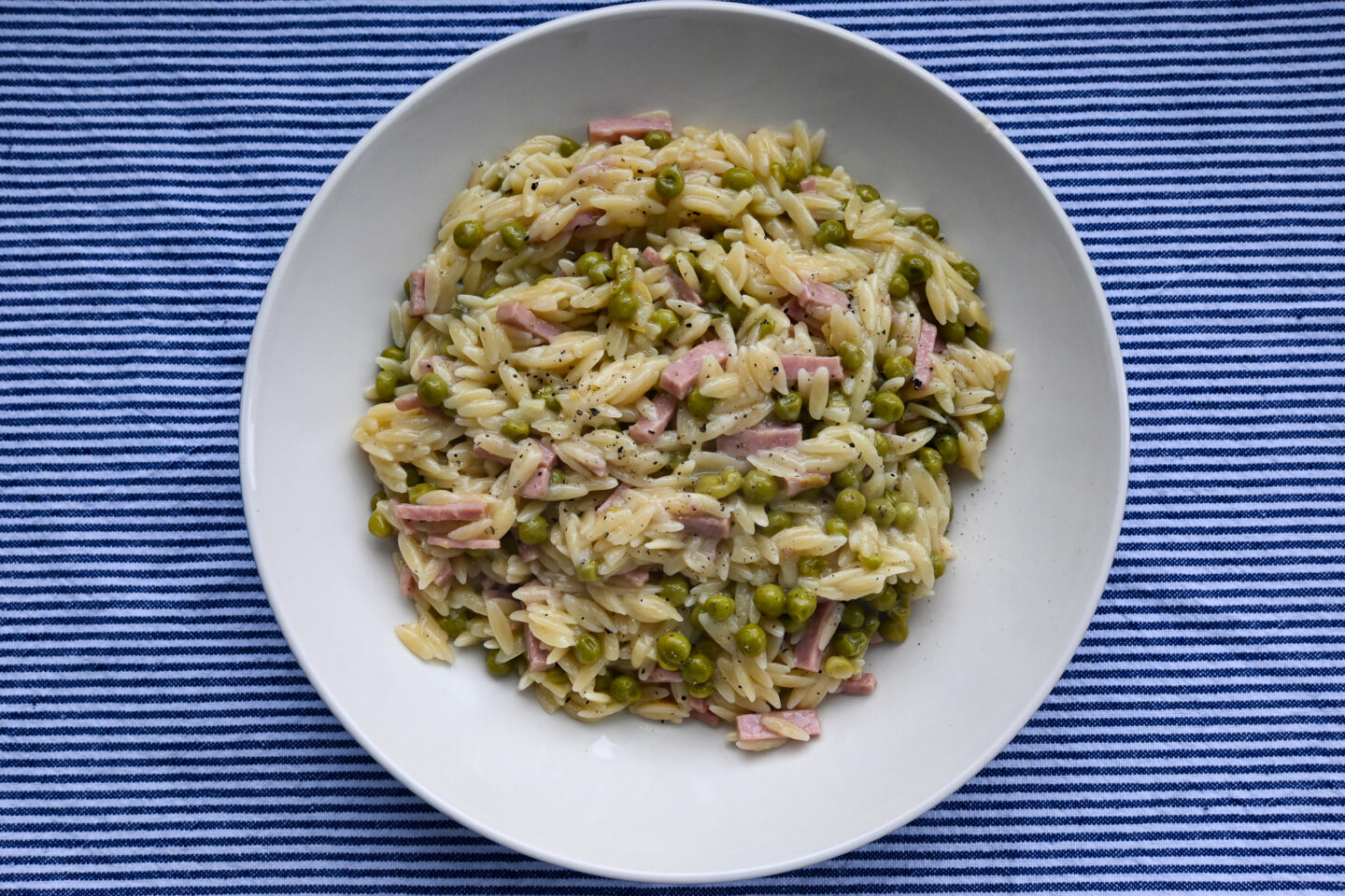 bowl of orzo, ham cubes & peas on a blue and white striped background