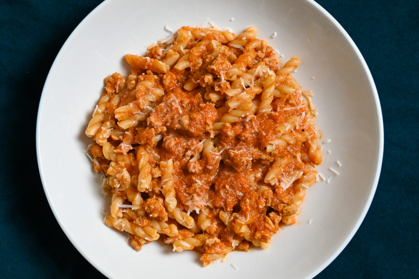 Gemelli Pasta With Chicken Bolognese Sauce sprinkled with Parmesan cheese over top on a white plate with a blue & white striped background