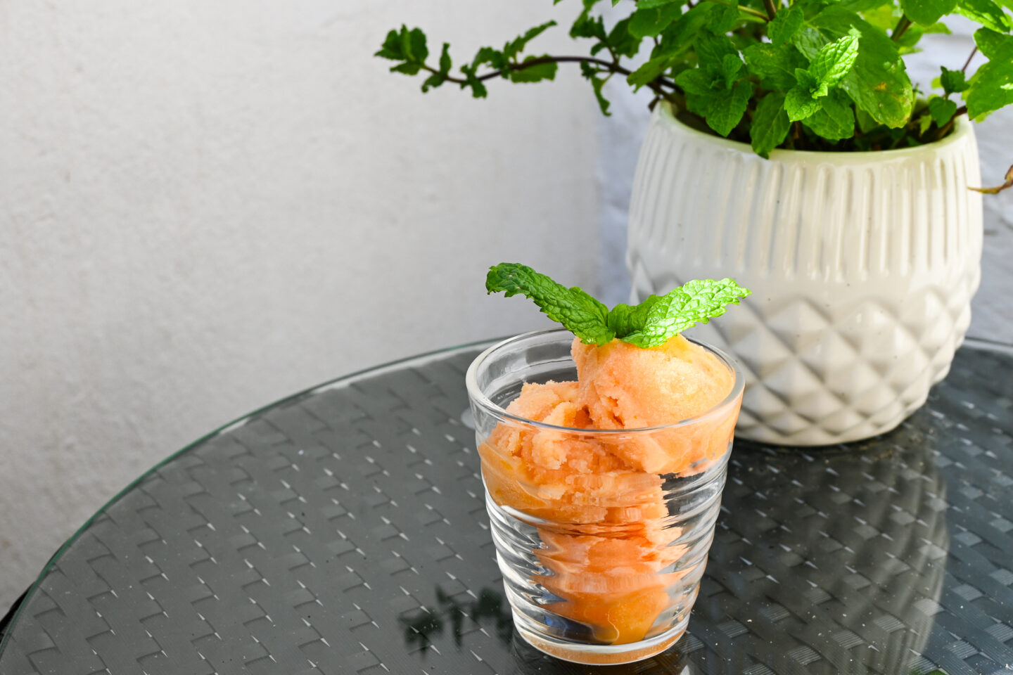 Grapefruit & Prosecco Sorbet in a clear glass (3 scoops) with a mint leaf garnish on a garden table next to a potted mint plant