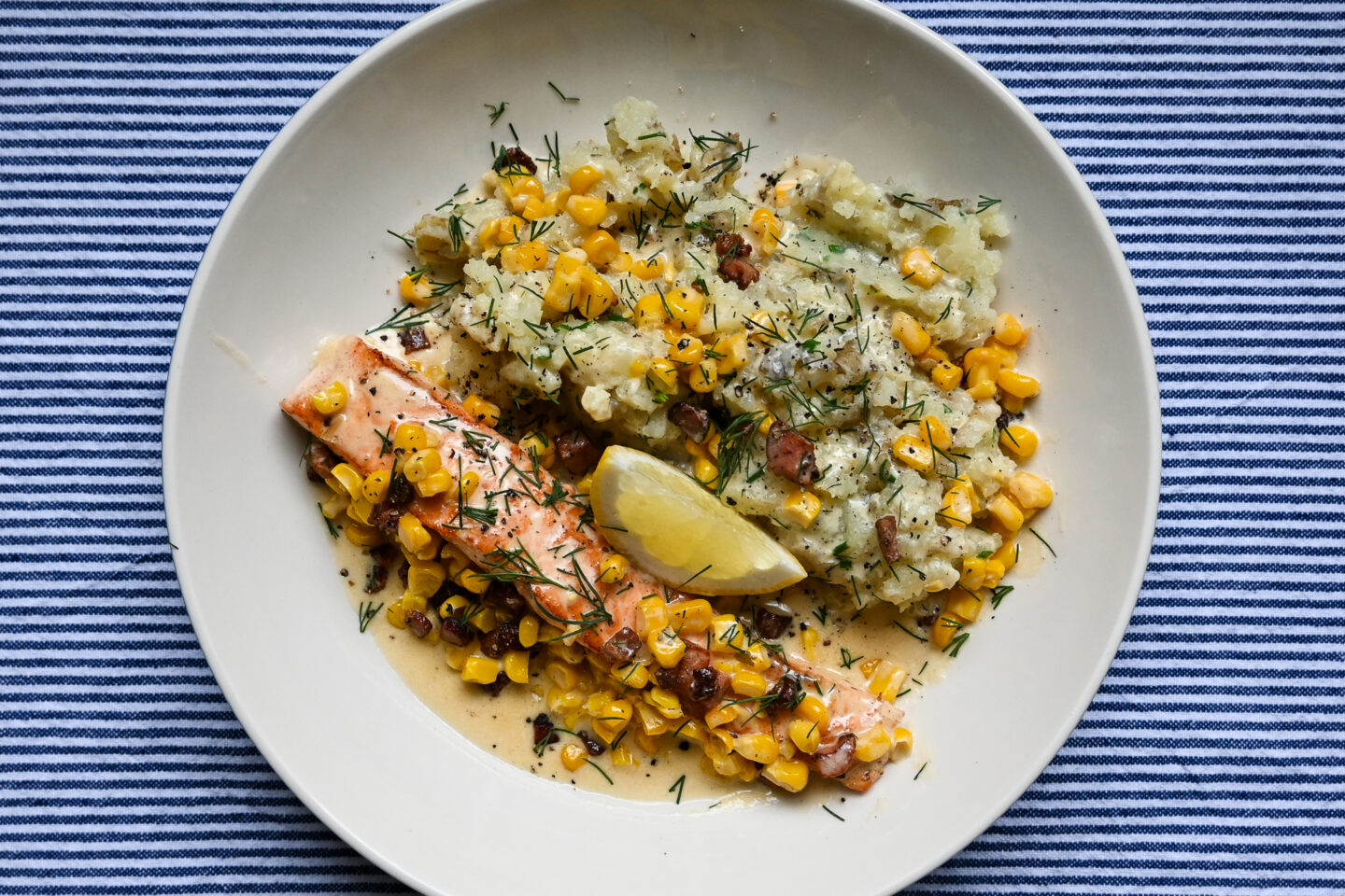 Salmon With Pancetta, Sweetcorn & Crushed Potatoes on a white plate with a blue & white striped background