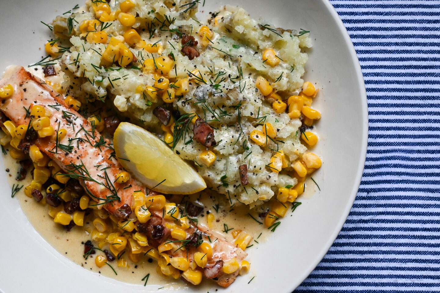 Salmon With Pancetta, Sweetcorn & Crushed Potatoes on a white plate with a blue & white striped background