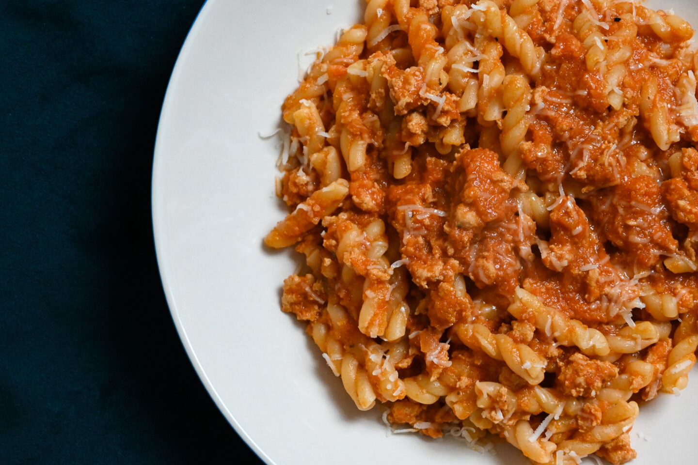 Gemelli Pasta With Chicken Bolognese Sauce sprinkled with Parmesan cheese over top on a white plate with a blue & white striped background