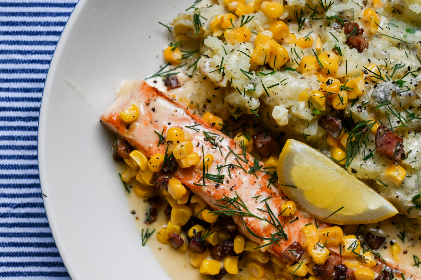 Salmon With Pancetta, Sweetcorn & Crushed Potatoes on a white plate with a blue & white striped background