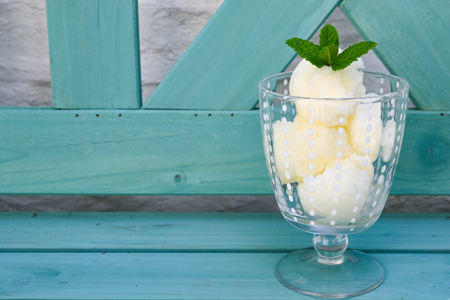 Parfait glass with scoops of Fizzy Lemon Sorbet topped with a mint leaf sprig sitting on a turquoise park bench