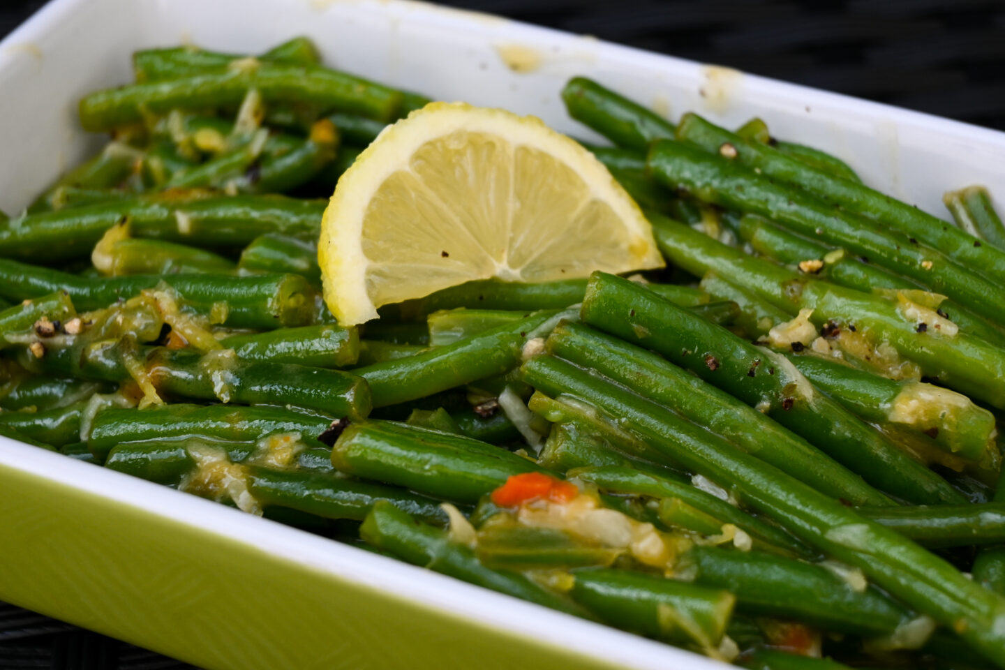 Green beans with glossy lemon butter sauce & lemon zest topped with a lemon wedge in a lime green serving dish