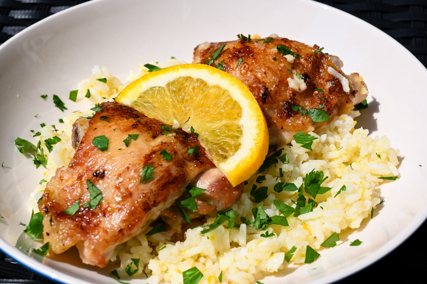 2 chicken thighs with browned, crispy skins on a bed of orange rice sprinkled with chopped parsley and garnished with an orange slice