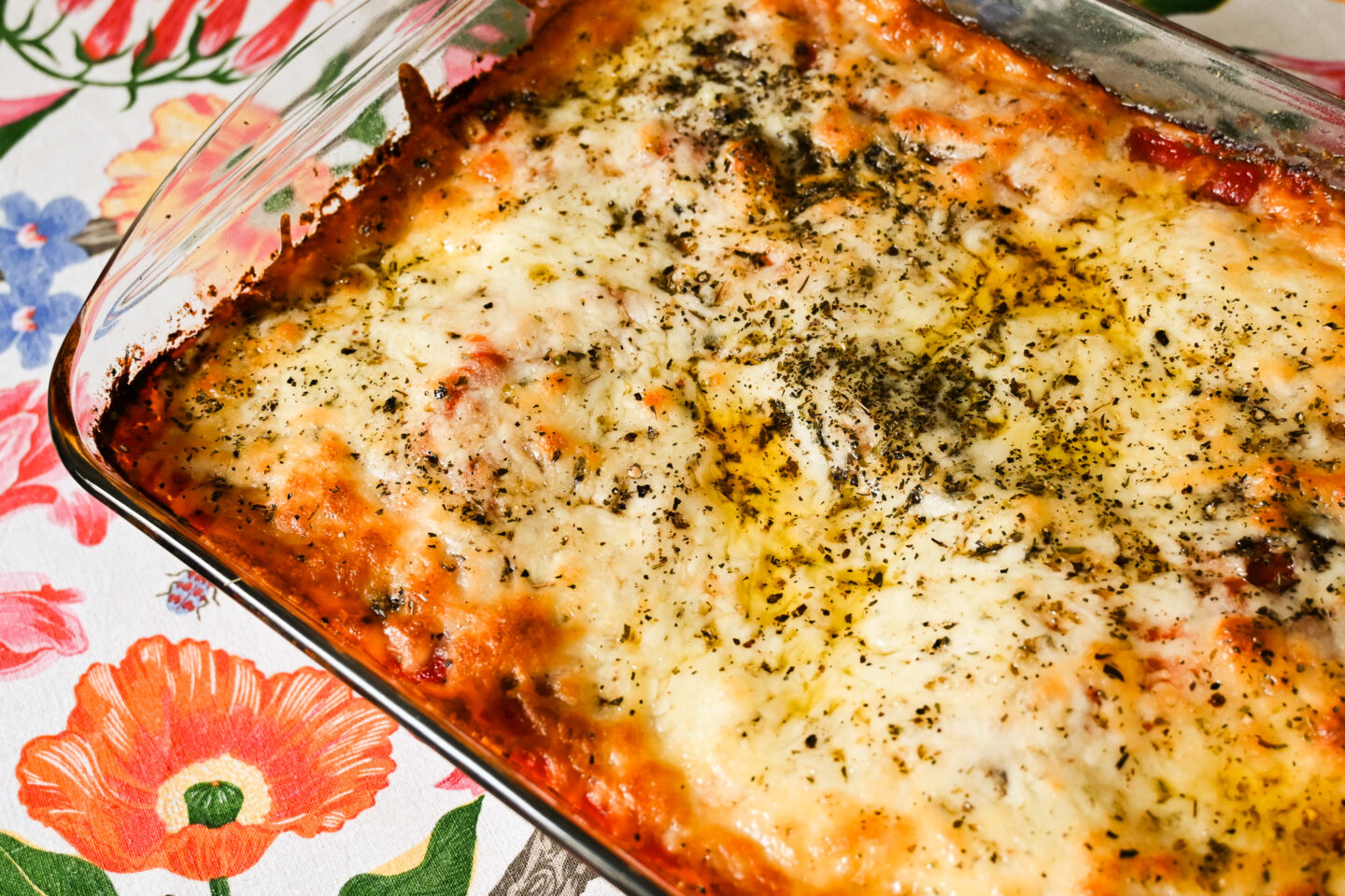 Pizza tortilla pie which looks a bit like lasagna in a glass casserole dish on a floral tablecloth