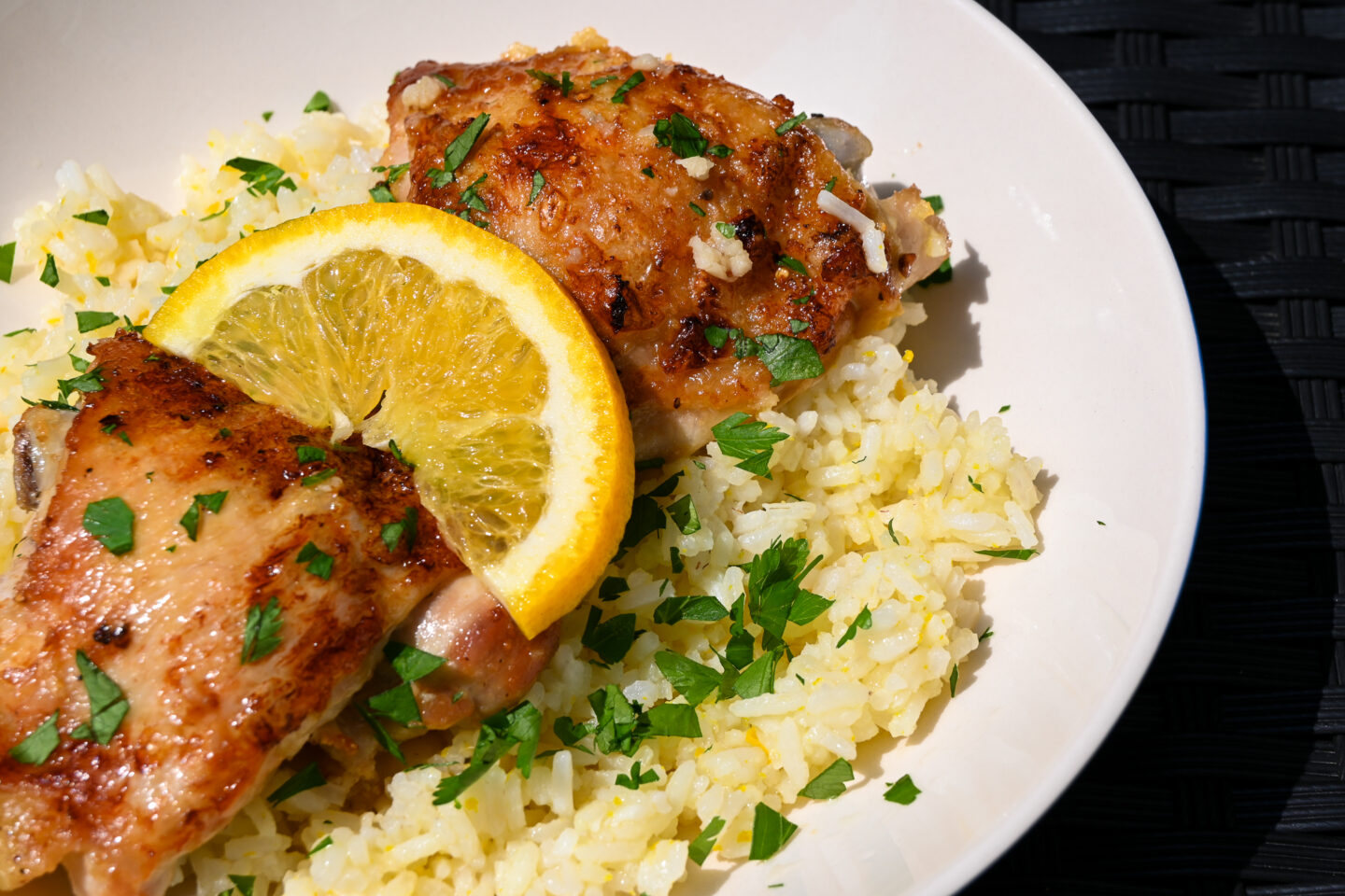 2 chicken thighs with browned, crispy skins on a bed of orange rice sprinkled with chopped parsley and garnished with an orange slice