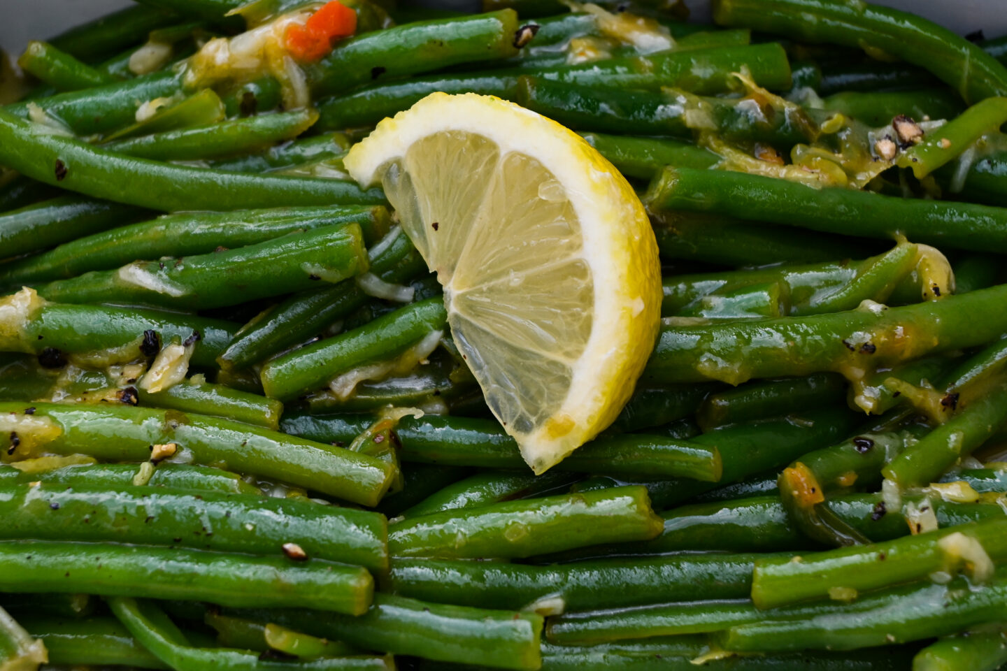 Green beans with glossy lemon butter sauce & lemon zest topped with a lemon wedge in a lime green serving dish