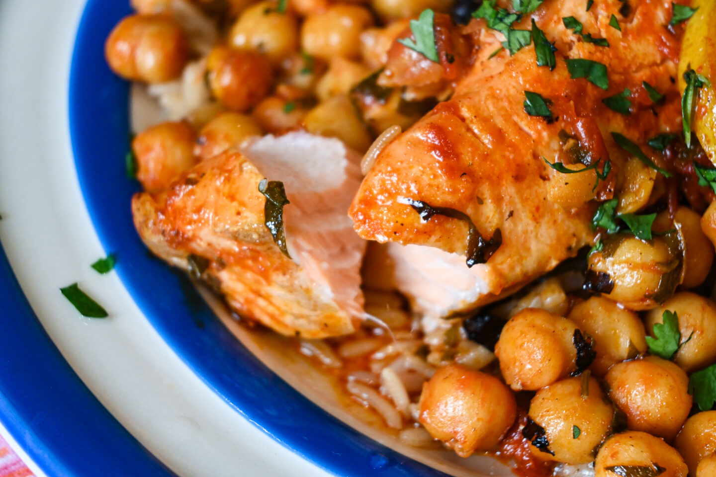 Close up of flaking salmon fillet with chickpeas in harissa & paprika sauce on brown rice