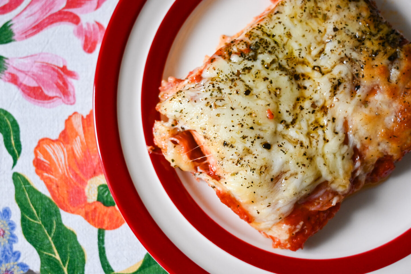 Pizza tortilla pie slice which looks a bit like lasagna in a glass casserole dish on a floral tablecloth