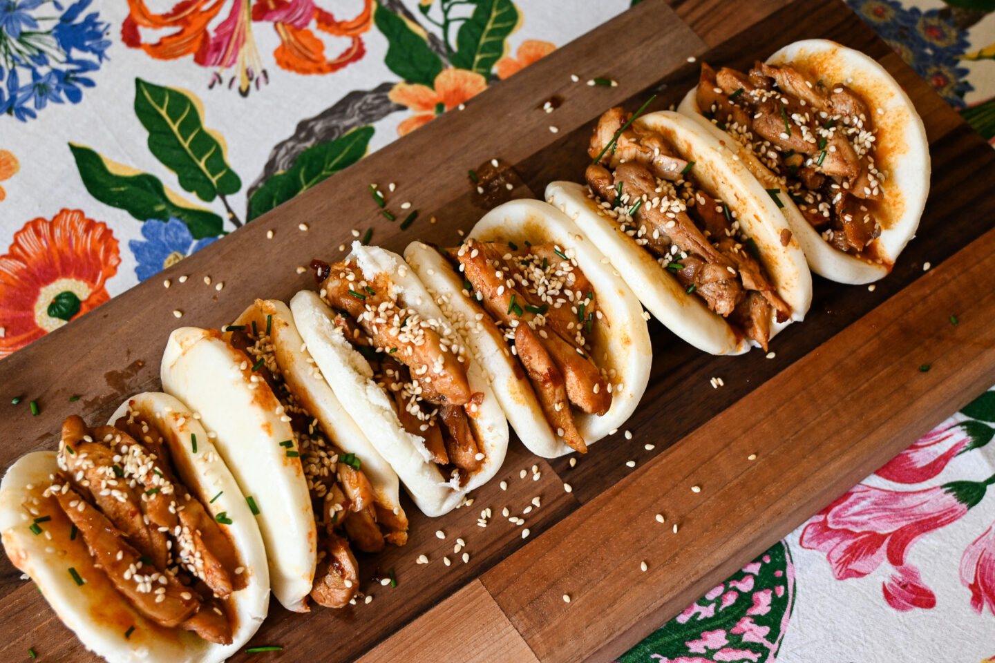 Honey, Soy & Harissa Chicken Bao Buns on a wooden chopping board with a floral background