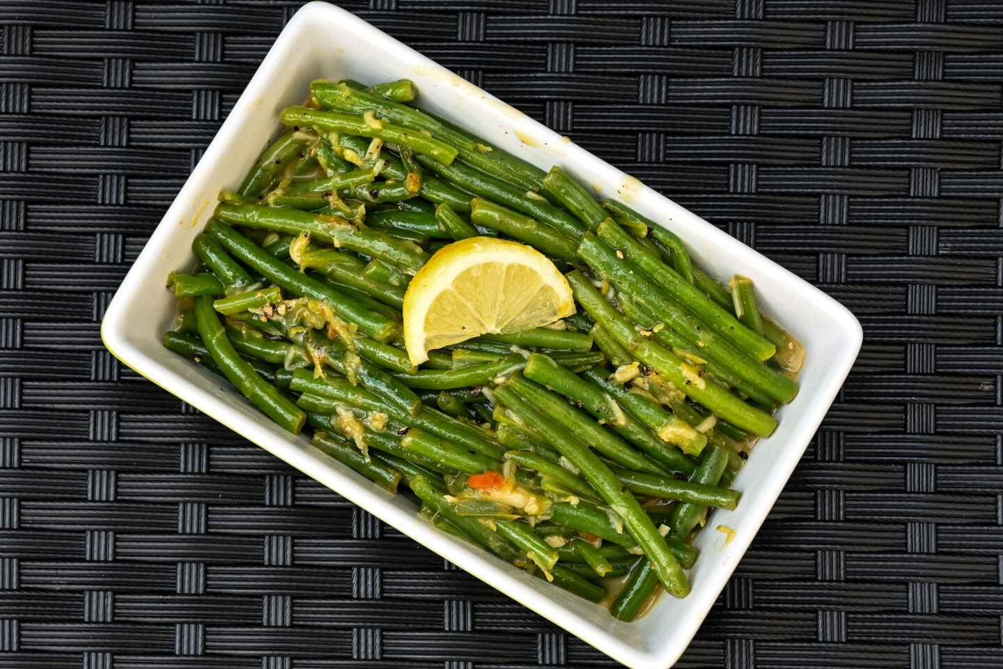 Green beans with glossy lemon butter sauce & lemon zest topped with a lemon wedge in a lime green serving dish