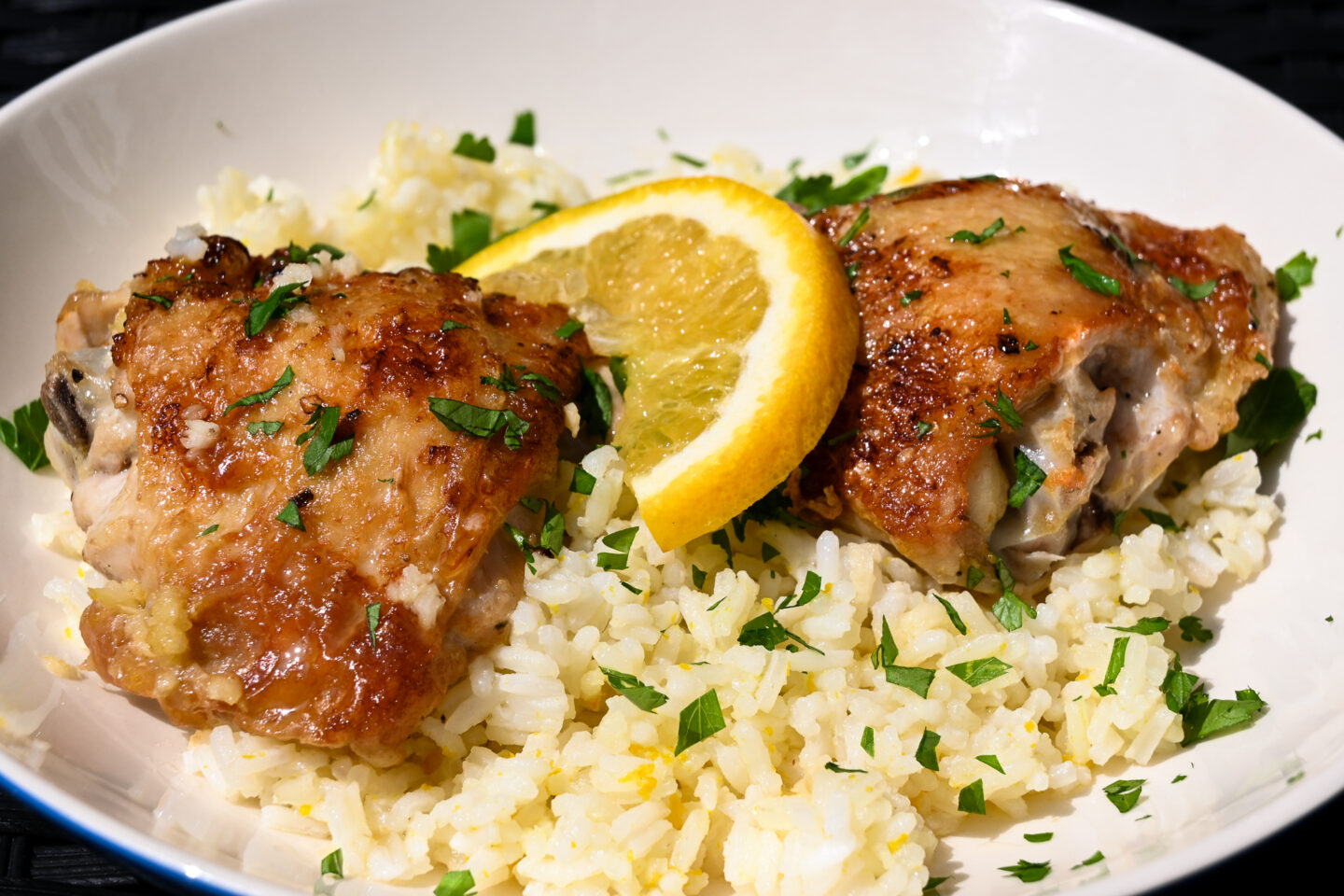 2 chicken thighs with browned, crispy skins on a bed of orange rice sprinkled with chopped parsley and garnished with an orange slice