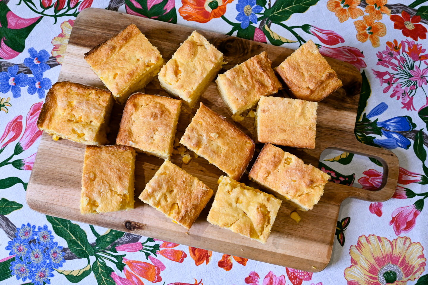 Squares of cornbread on a cutting board with a floral tablecloth background