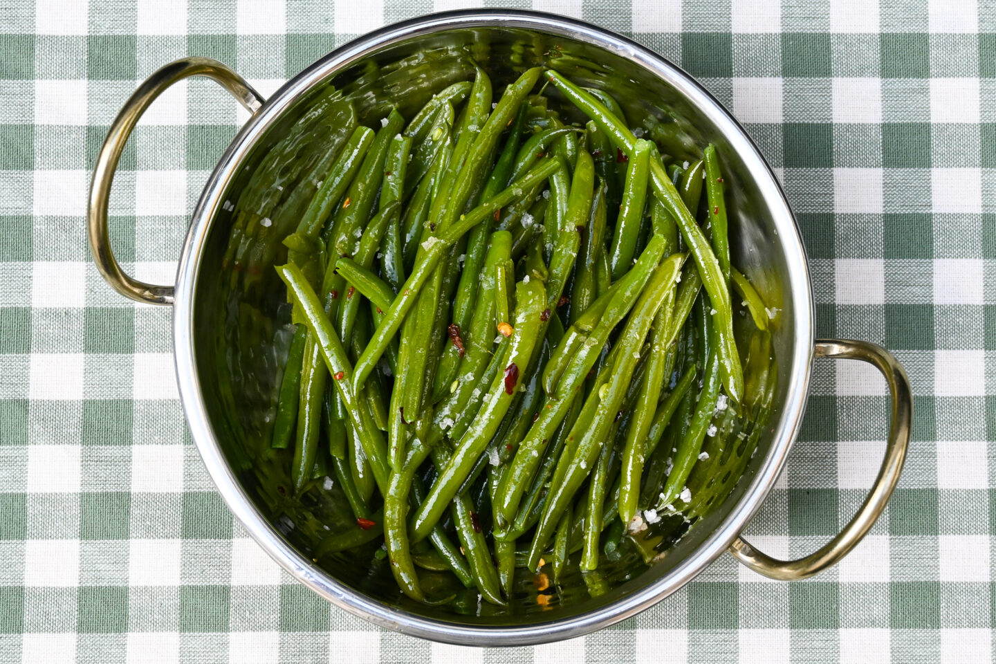 Chilli Garlic Green Beans sprinkled with sea salt i a metal bowl on a light green & white gingham background