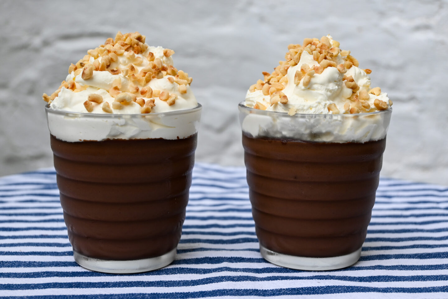 Small clear glasses filled with chocolate pudding topped with whipped cream and toasted chopped hazelnuts