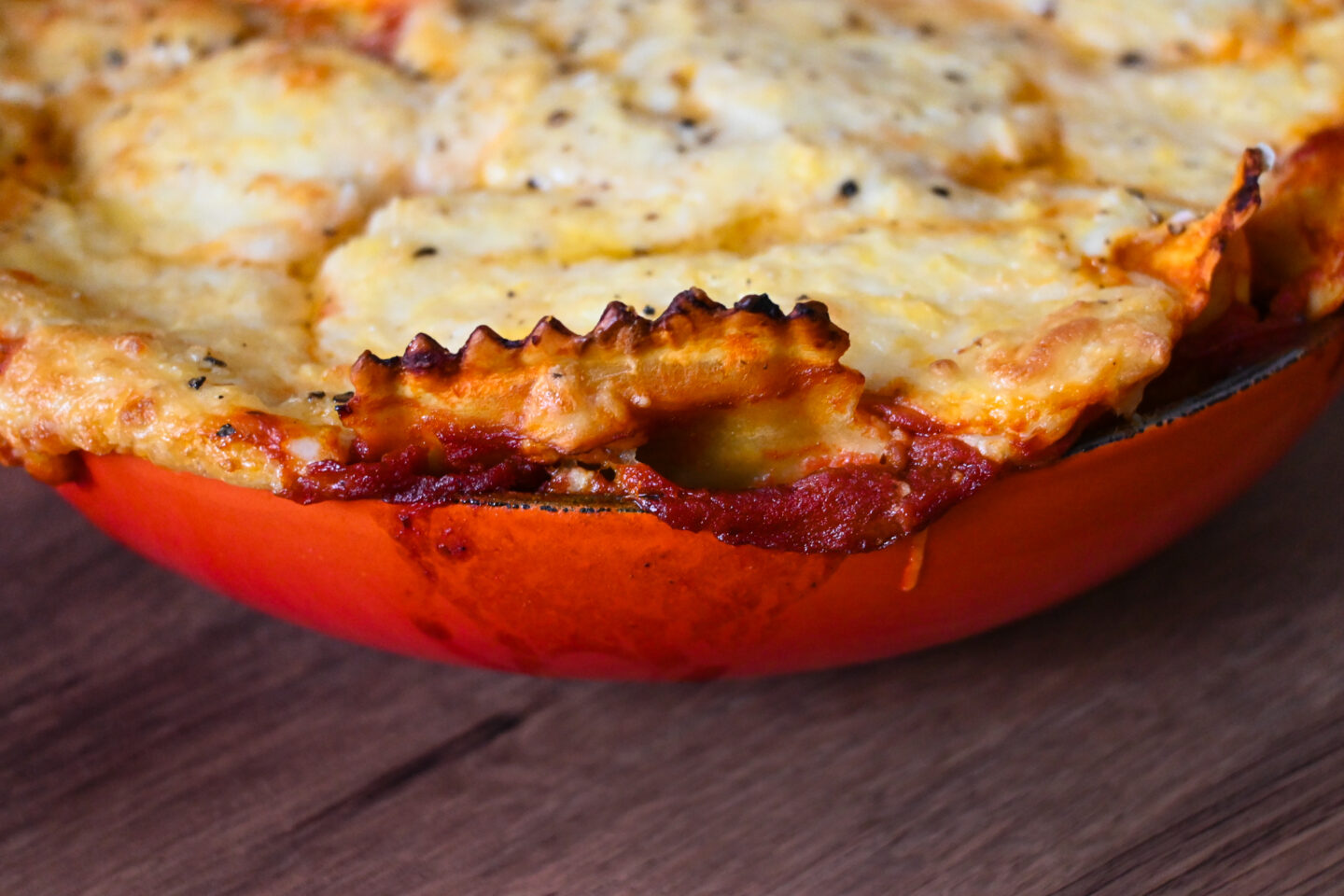 Orange Le Creuset Cast Iron Casserole with cheesy baked ravioli coming over the edge.