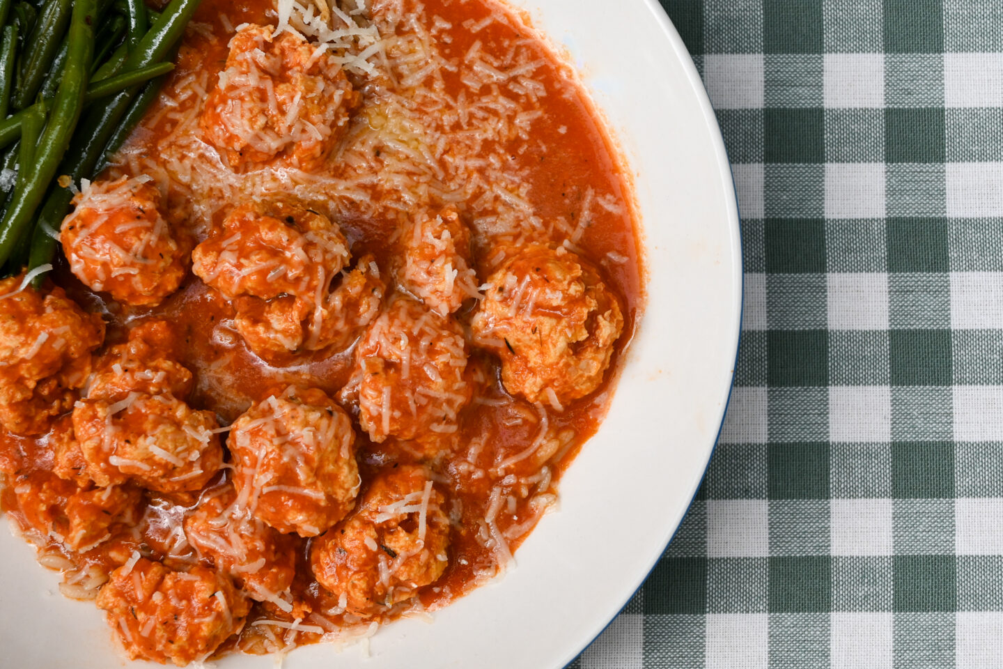 Turkey meatballs in a tomato sauce over brown rice with green beans on a green & white checked background