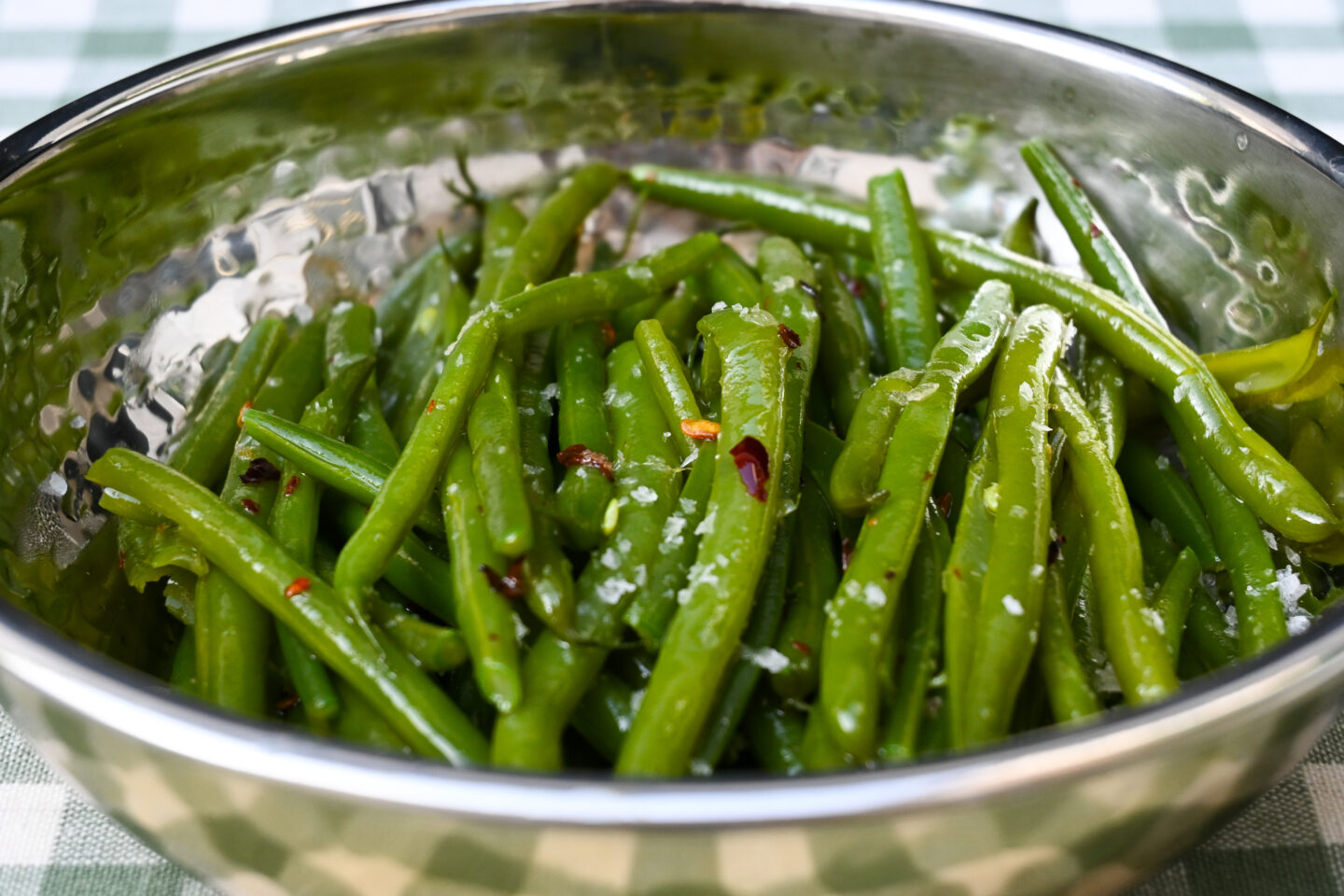 Chilli Garlic Green Beans sprinkled with sea salt i a metal bowl on a light green & white gingham background closeup
