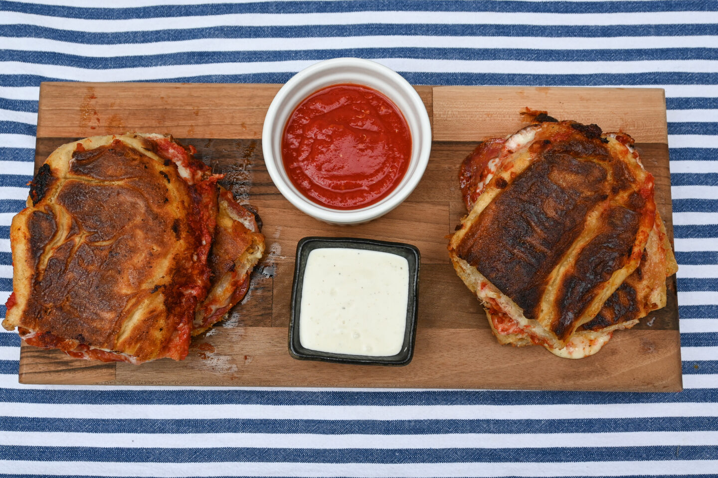 Two Pepperoni Pizza Paninis on a wooden serving board with pizza sauce & ranch dressing for dipping