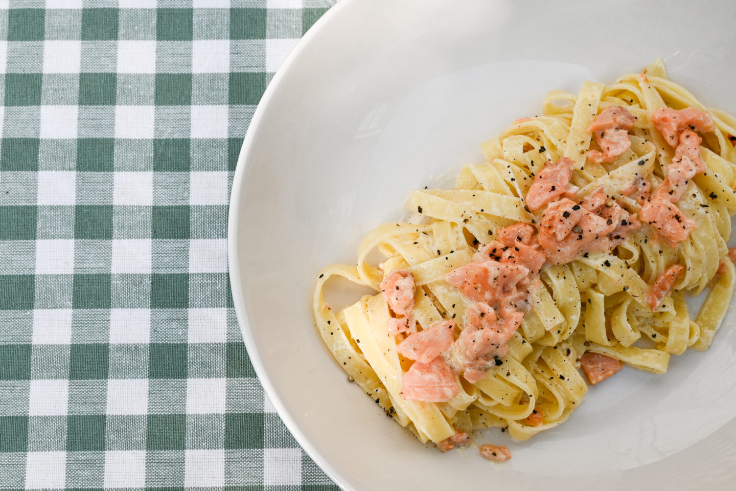 Tagliatelle with smoked salmon whisky cream sauce in a bowl on a green & white checked background