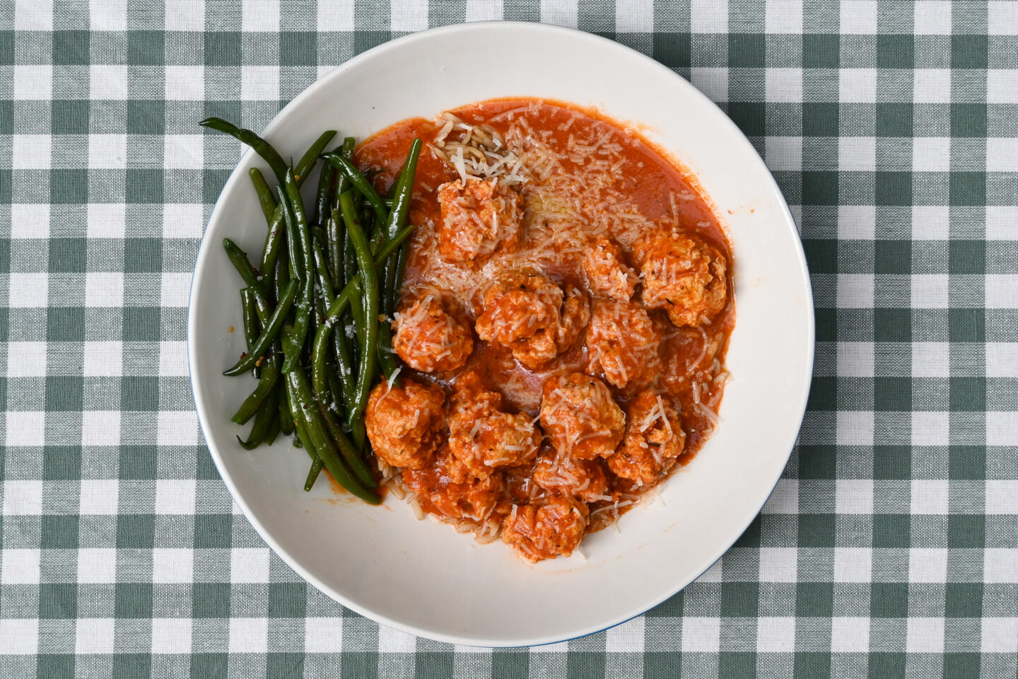 Turkey meatballs in a tomato sauce over brown rice with green beans on a green & white checked background