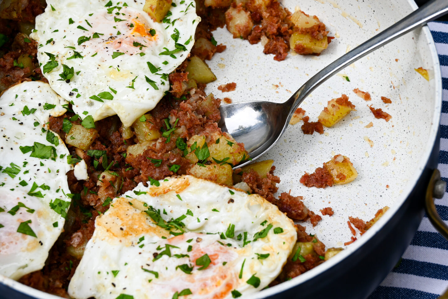 Corned Beef Hash topped with Fried Eggs and Sprinkled chopped parsley in a skillet with a serving spoon