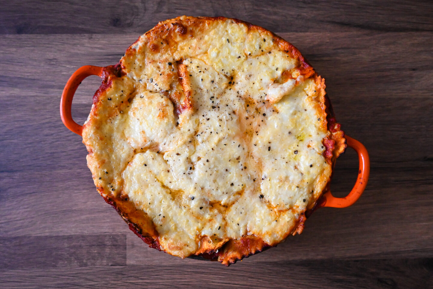 Cheesy Baked Ravioli in an orange casserole on a wooden table