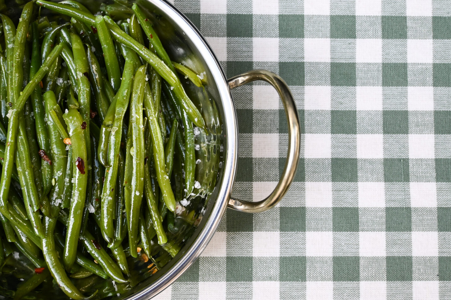 Chilli Garlic Green Beans sprinkled with sea salt i a metal bowl on a light green & white gingham background