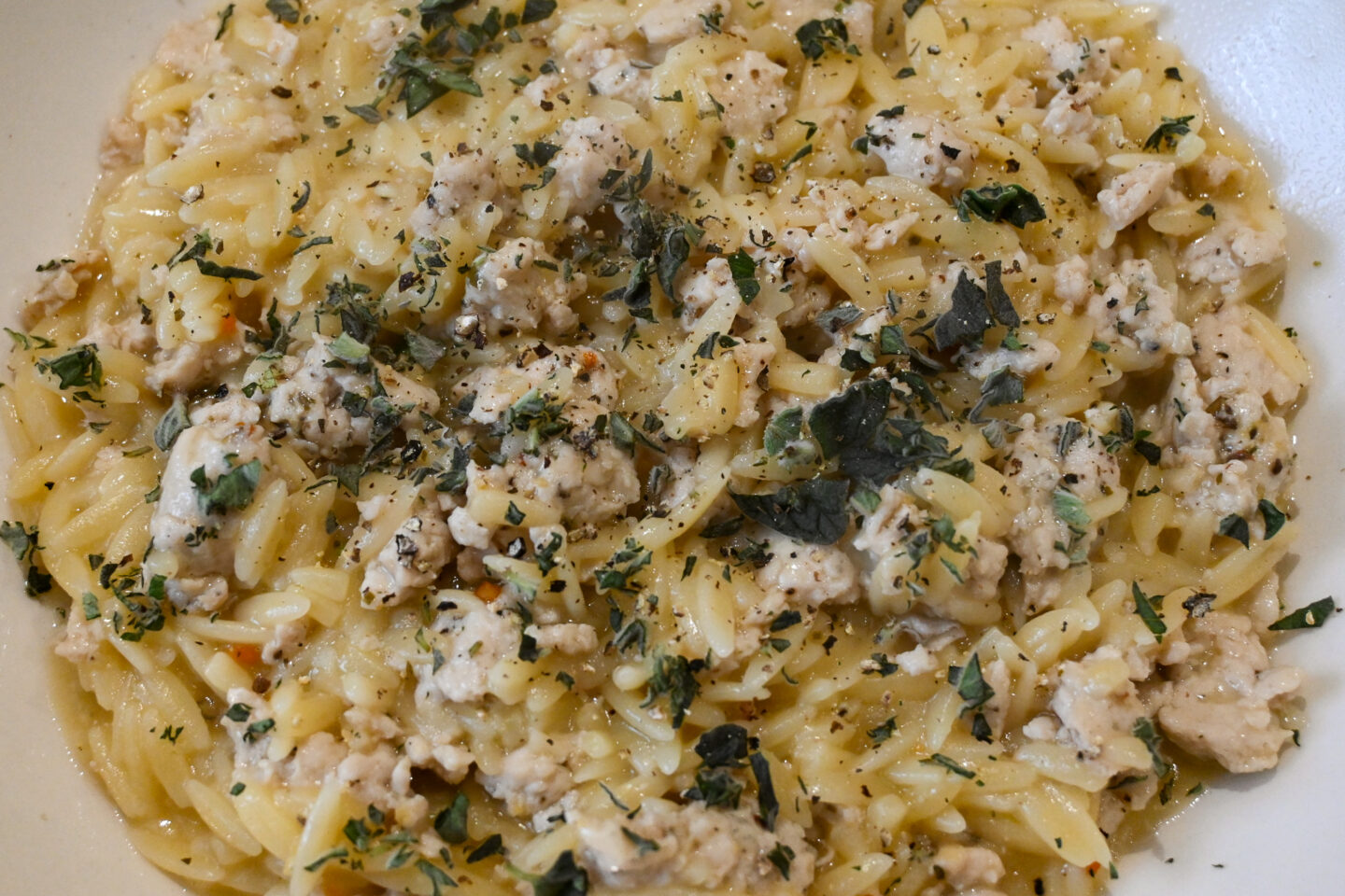 Lemon Oregano Chicken Orzo in a white Bowl on a Wooden Table Closeup