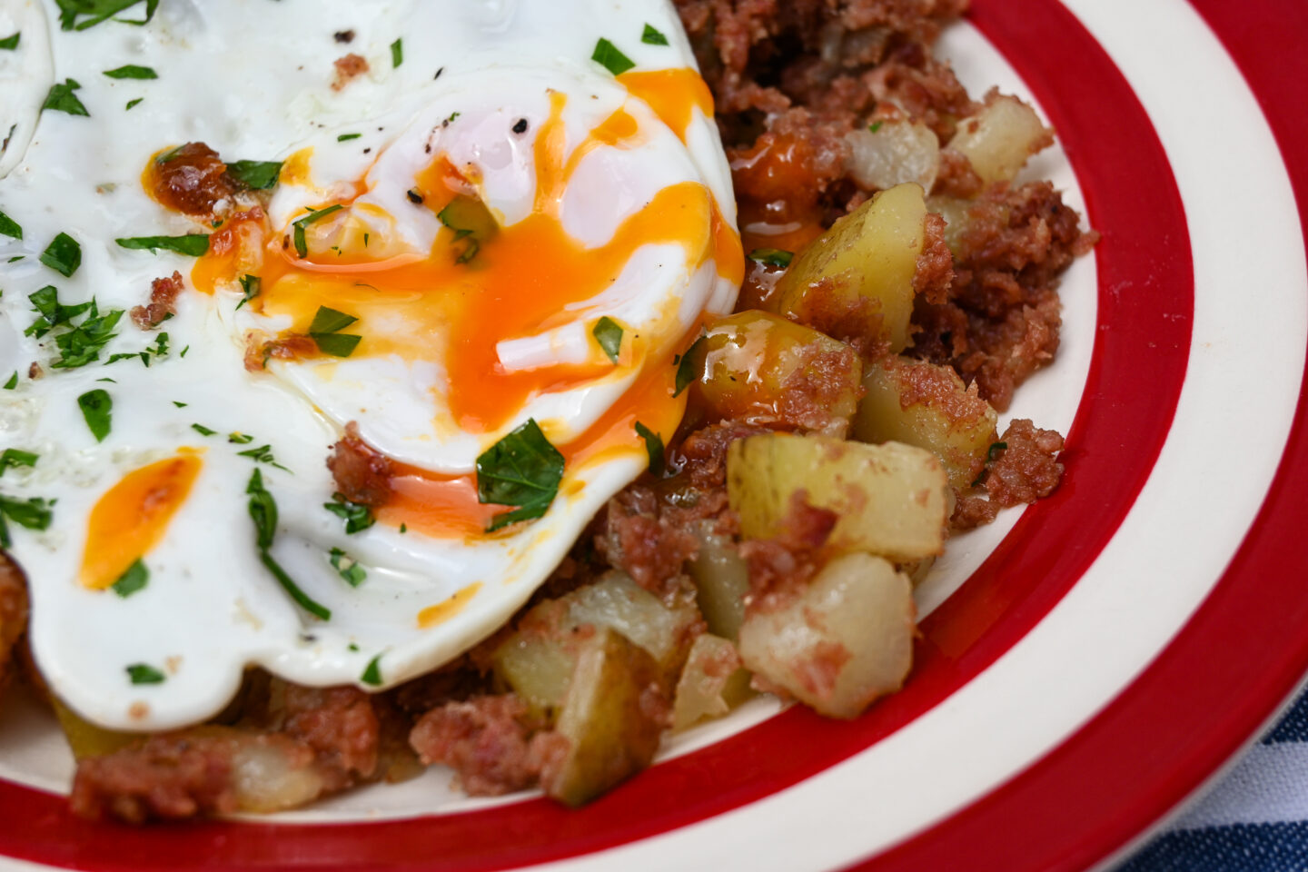 Runny egg closeup on top of corned beef hash on a red & white striped plate