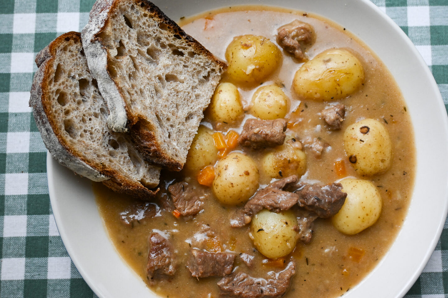 White wine & dijon beef stew with carrots & potatoes served in a white wide bowl with two slices of sourdough bread