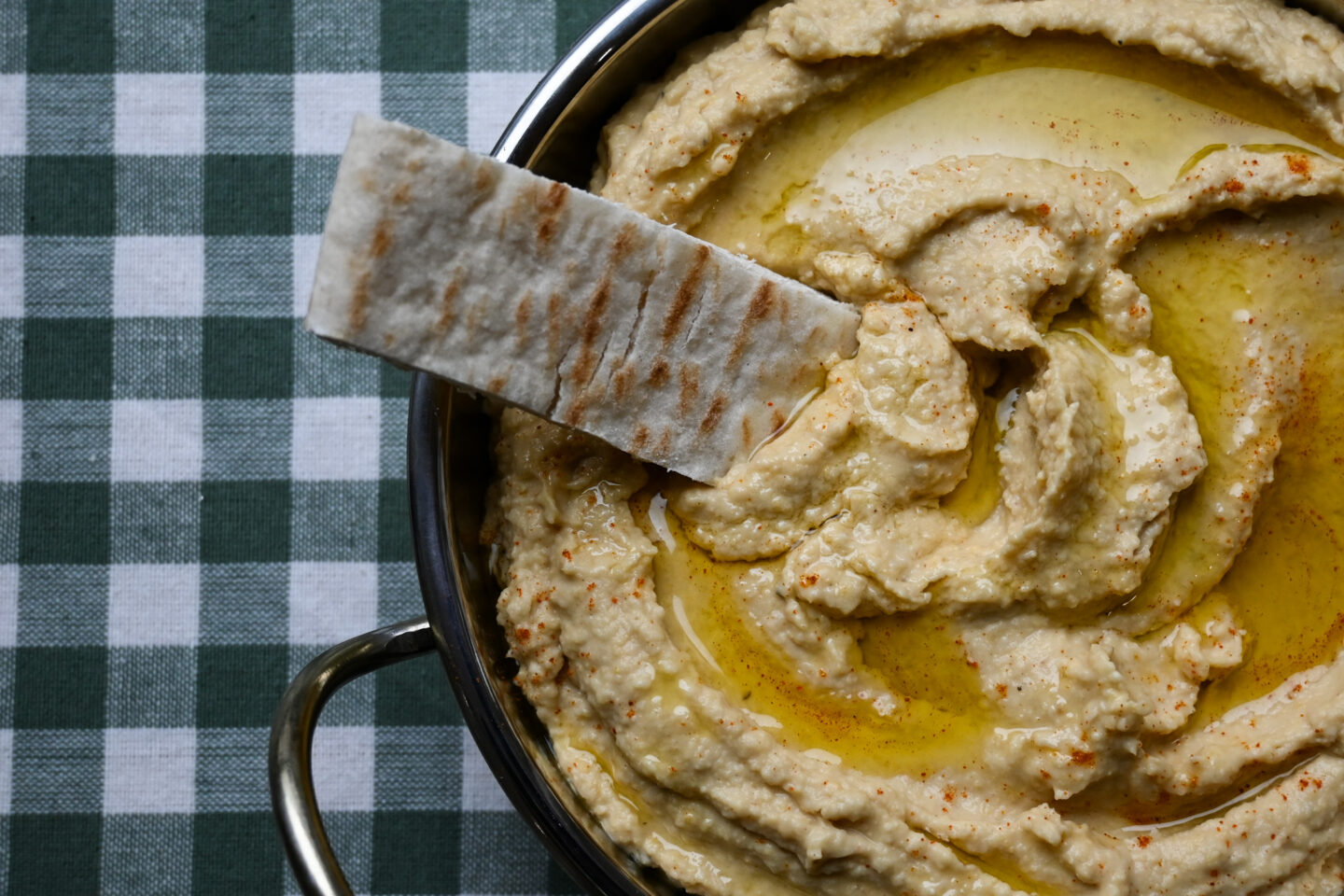 Close-up of Roasted Garlic & Lemon Hummus with a pitta bread strip dipped in.