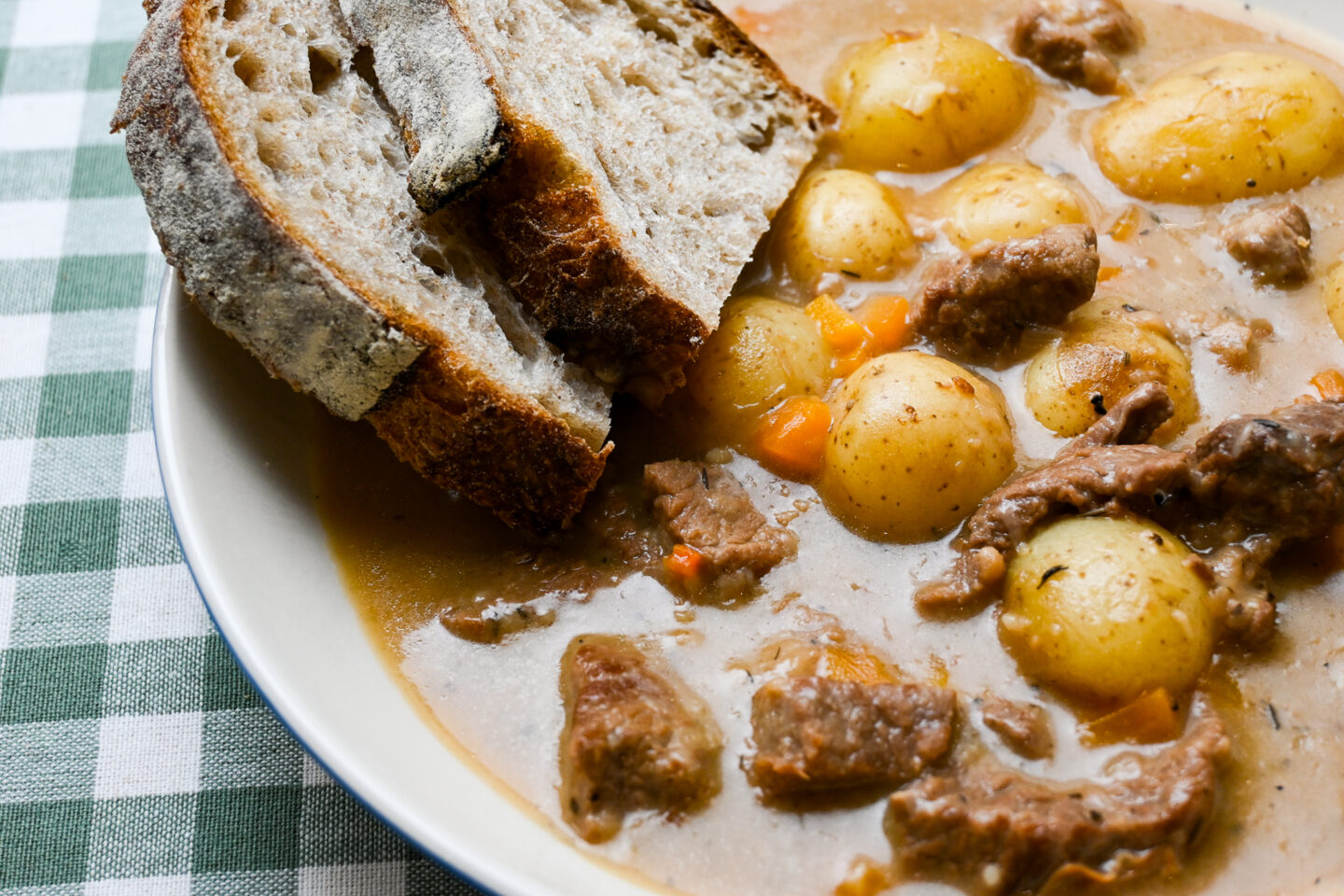 White wine & dijon beef stew with carrots & potatoes served in a white wide bowl with two slices of sourdough bread closeup