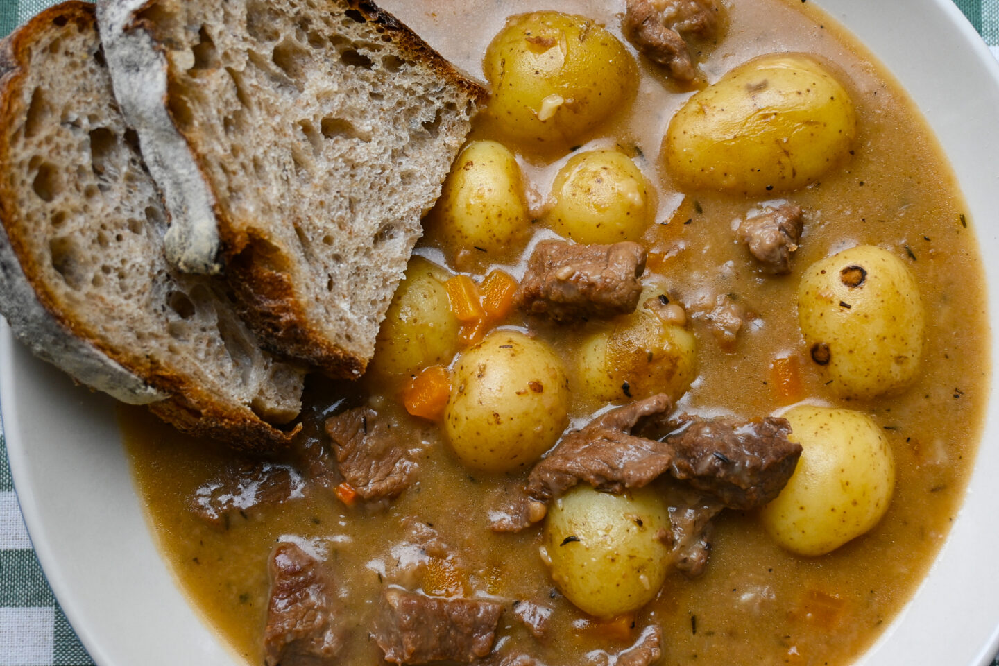 White wine & dijon beef stew with carrots & potatoes served in a white wide bowl with two slices of sourdough bread