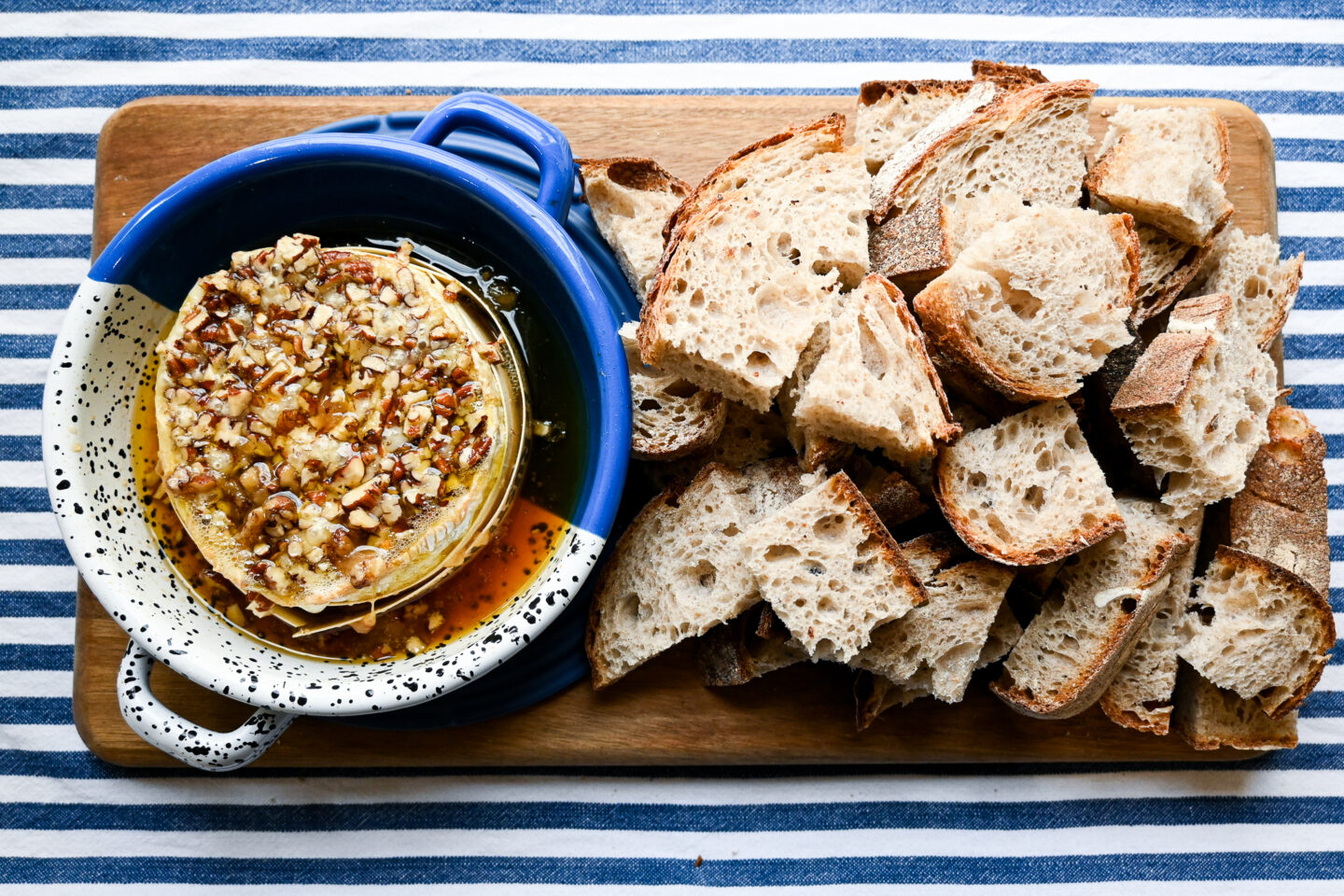 Grazing board with Maple Pecan Baked Camembert and bread on a wooden board sitting on a blue & white striped tablecloth