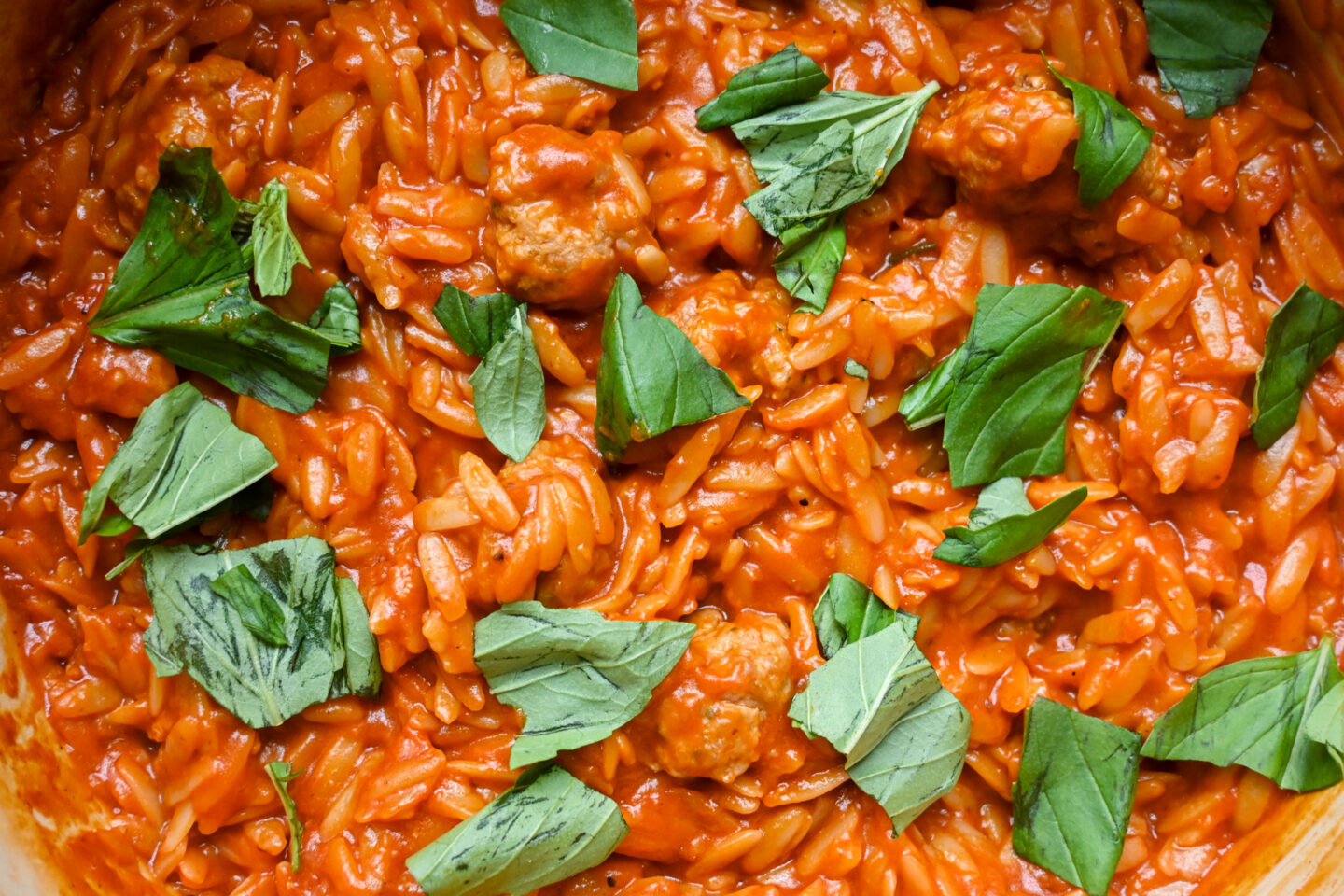 One Pot Sausages Meatballs With Orzo in a tomato sauce sprinkled with torn basil leaves Closeup