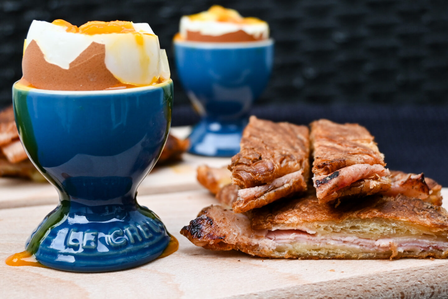 Blue Le Creuset egg cups With dripping soft boiled eggs and ham & cheese croissant dippers on the side