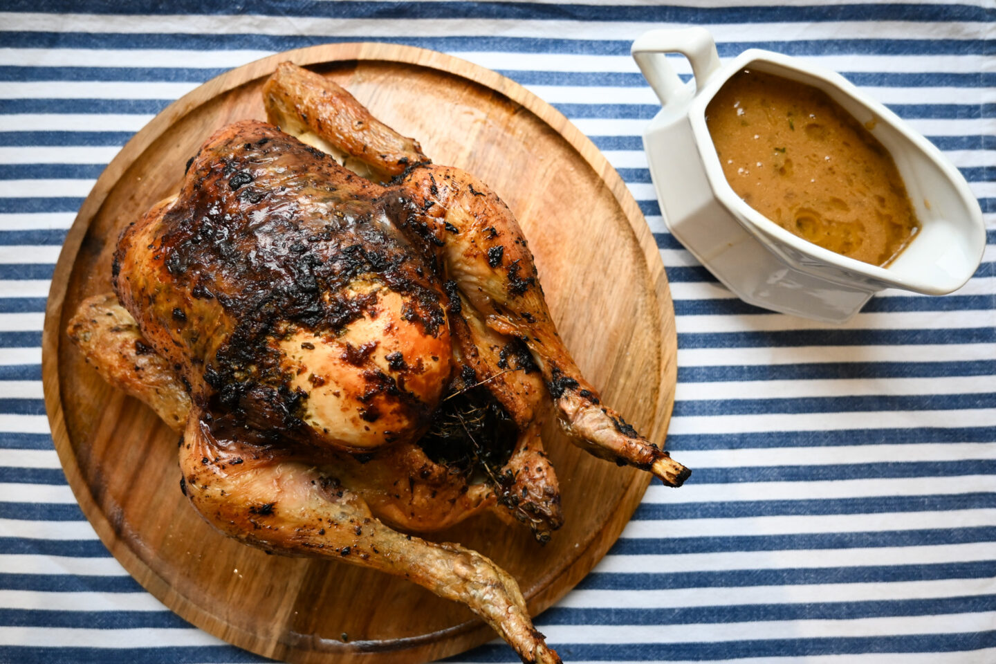 Garlic Butter Roast Chicken on a wooden tray next to a gravy boat of gravy
