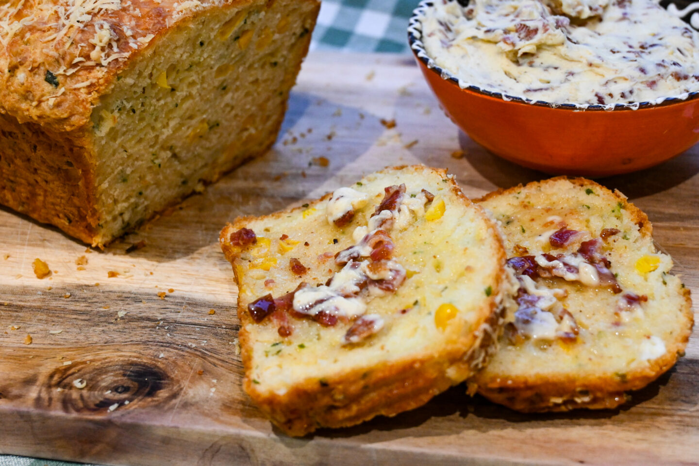 2 Slices of Corny Cheese Bread Loaf Smeared With Bacon Butter in front of a bowl of bacon butter and the cut loaf of bread