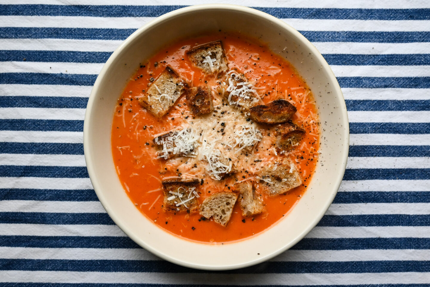 Bowl of Cream of Tomato Soup garnished with homemade sourdough croutons, fresh black pepper and grated Parmesan cheese