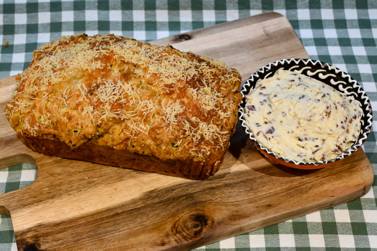 Loaf of Corny Cheese Bread on a cutting board with a bowl of bacon butter