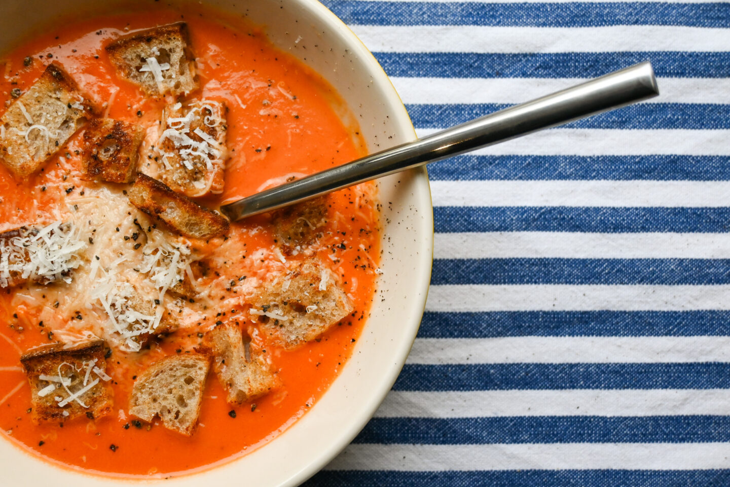 Bowl of Cream of Tomato Soup garnished with homemade sourdough croutons, fresh black pepper and grated Parmesan cheese