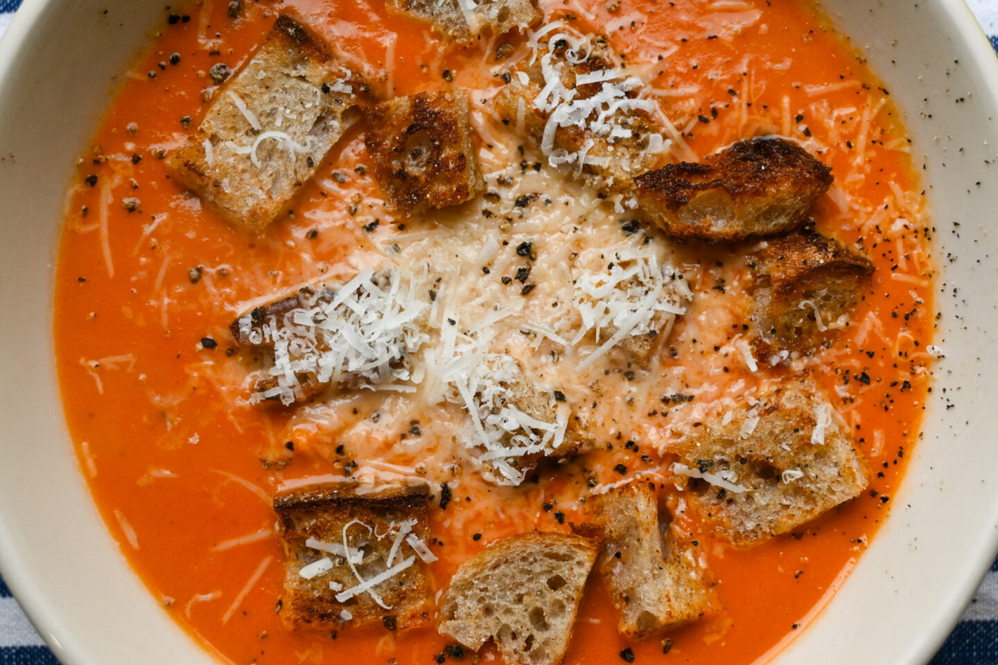 Bowl of Cream of Tomato Soup garnished with homemade sourdough croutons, fresh black pepper and grated Parmesan cheese closeup
